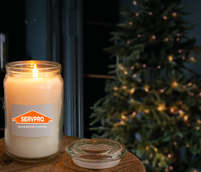 Lit candle with SERVPRO logo in front of a decorated Christmas tree